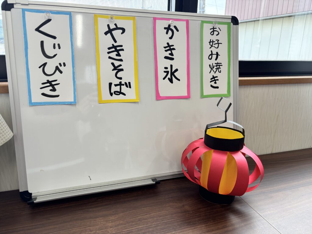 ホワイトボードにかき氷、焼きそば、お好み焼き、くじびきの札が貼ってあります。