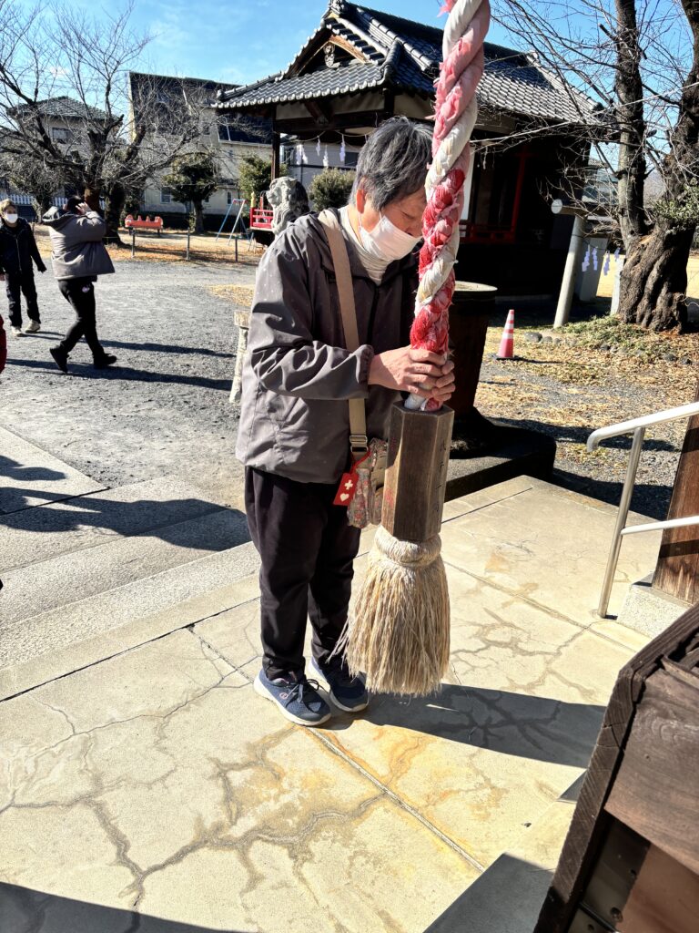 女性の利用者さんが神社をお参りしているところを社殿側から撮影。背景に神楽殿がある。